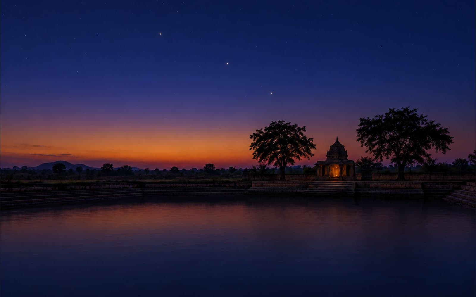 Three bright planets in the blue-hour sky over a temple tank in India